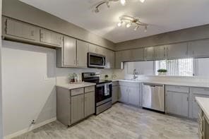 kitchen with light hardwood / wood-style floors, appliances with stainless steel finishes, track lighting, and gray cabinetry