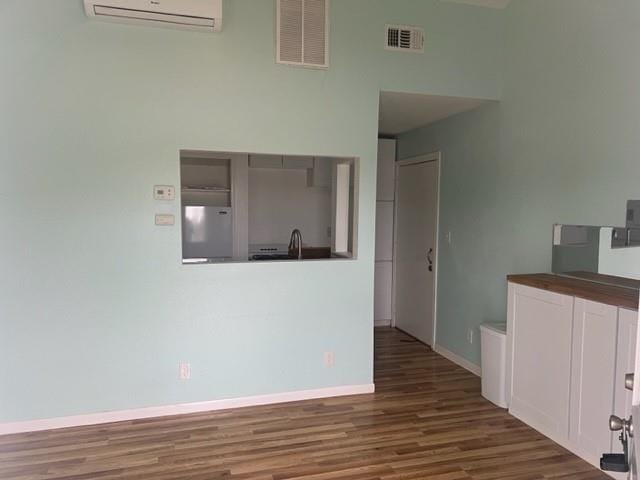 interior space with baseboards, visible vents, dark wood-style flooring, and a wall mounted air conditioner