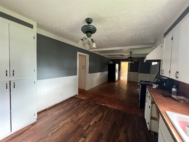 kitchen with beamed ceiling, white cabinets, hardwood / wood-style flooring, stainless steel refrigerator, and ceiling fan