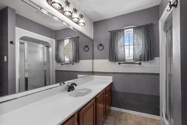 bathroom featuring a shower with door, tile walls, vanity, a textured ceiling, and tile patterned floors