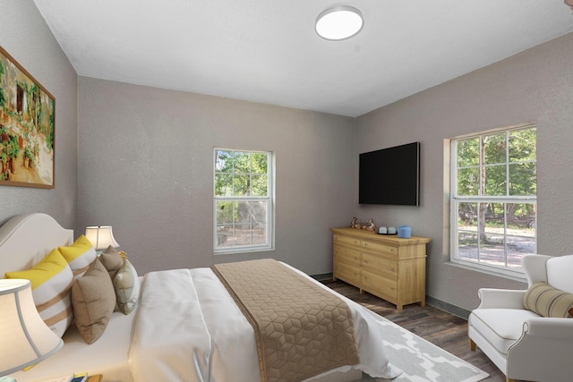 bedroom with baseboards, dark wood-type flooring, and a textured wall