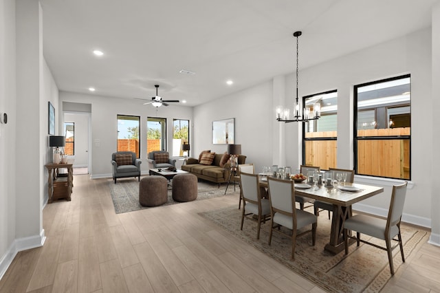 dining space with ceiling fan with notable chandelier and light hardwood / wood-style flooring