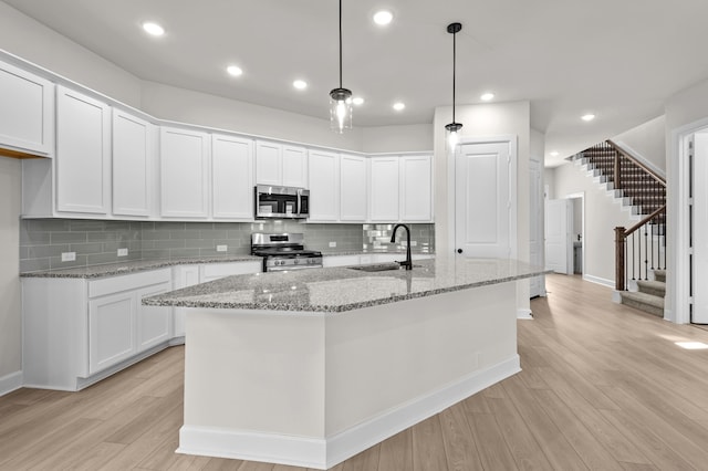 kitchen with a center island with sink, white cabinetry, appliances with stainless steel finishes, and light hardwood / wood-style flooring