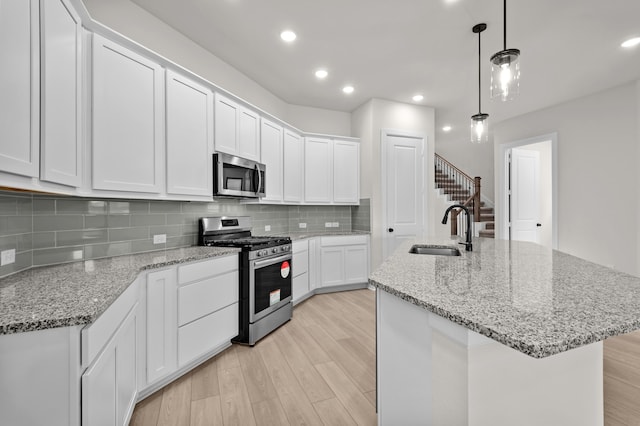 kitchen featuring appliances with stainless steel finishes, sink, pendant lighting, a center island with sink, and white cabinets