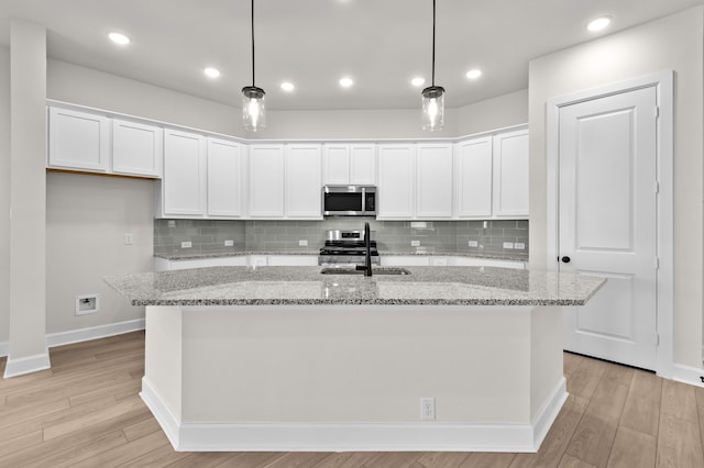 kitchen featuring a center island with sink, white cabinets, decorative light fixtures, and appliances with stainless steel finishes