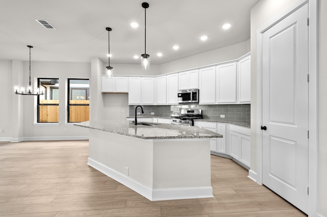 kitchen with white cabinets, sink, an island with sink, appliances with stainless steel finishes, and decorative light fixtures