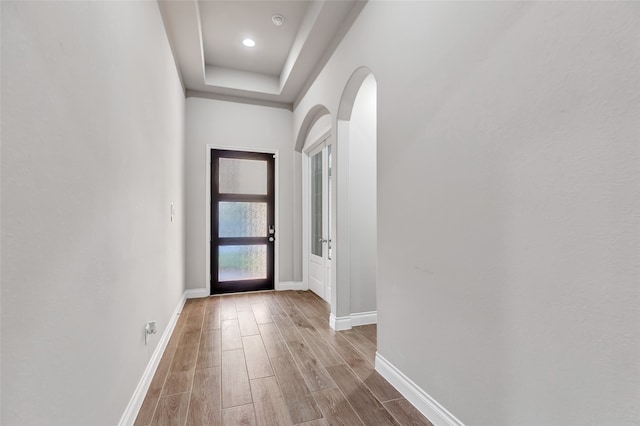 doorway to outside with a tray ceiling and light hardwood / wood-style flooring