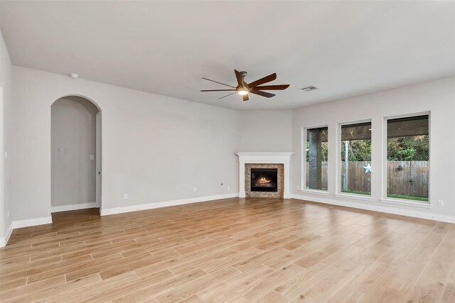 unfurnished living room featuring a stone fireplace, ceiling fan, and light hardwood / wood-style flooring