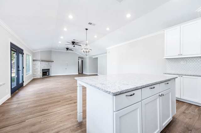 kitchen with a stone fireplace, crown molding, ceiling fan, and light hardwood / wood-style flooring