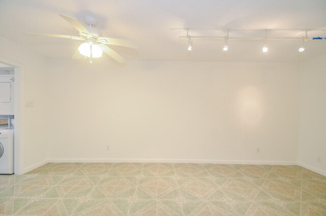 unfurnished room featuring stacked washer / drying machine, ceiling fan, and rail lighting