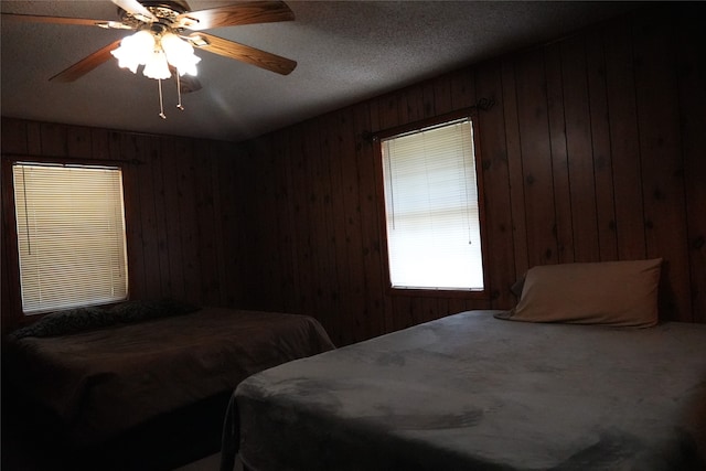 bedroom featuring wooden walls, a textured ceiling, and ceiling fan