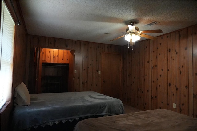 bedroom with visible vents, ceiling fan, a textured ceiling, wood walls, and a fireplace