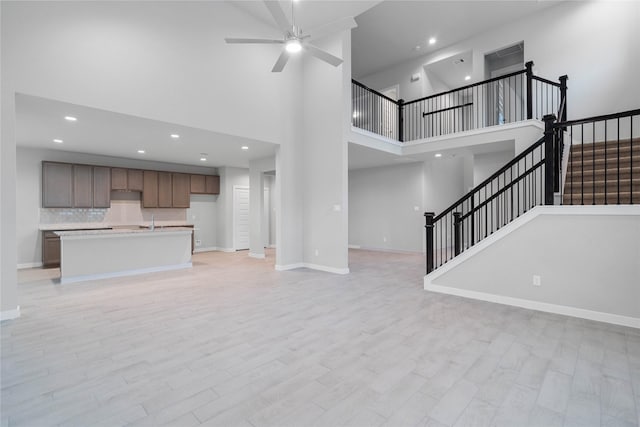 unfurnished living room with ceiling fan, a high ceiling, and light wood-type flooring