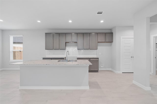 kitchen with an island with sink, light stone counters, and sink