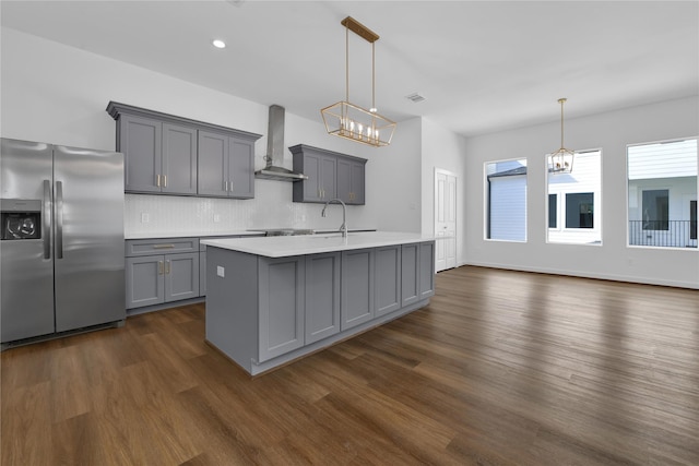 kitchen with wall chimney range hood, gray cabinets, hanging light fixtures, and stainless steel refrigerator with ice dispenser