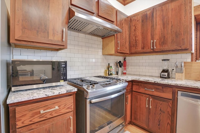 kitchen with tasteful backsplash, light stone counters, range hood, and appliances with stainless steel finishes