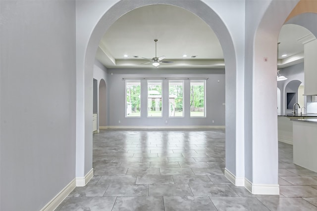 unfurnished living room featuring a tray ceiling, sink, ceiling fan, and light tile floors