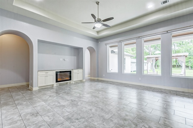 unfurnished living room with ceiling fan, a raised ceiling, and light tile floors