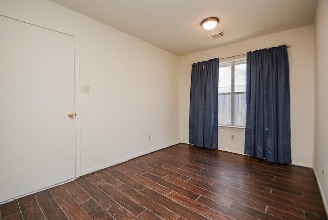 empty room featuring dark wood finished floors, visible vents, and baseboards