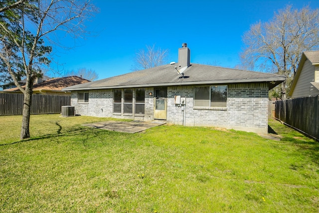 back of property with a fenced backyard, a chimney, central air condition unit, a lawn, and brick siding