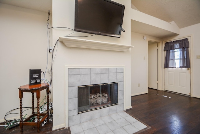 unfurnished living room with a tile fireplace, a textured ceiling, baseboards, and wood finished floors