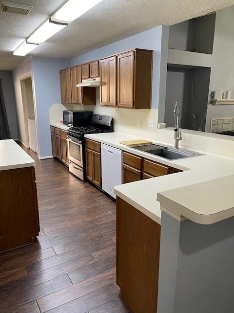 kitchen with a sink, a peninsula, black microwave, white dishwasher, and gas range