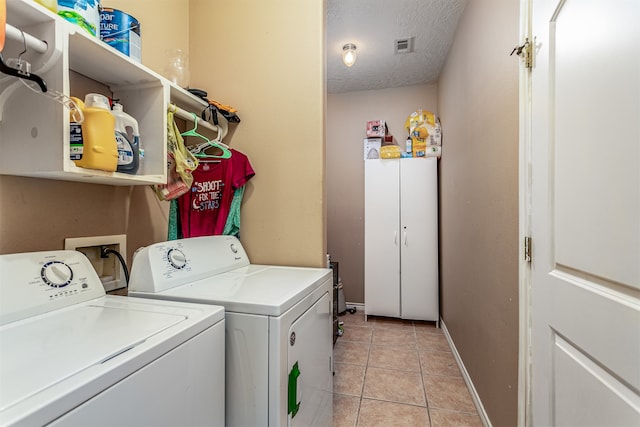 laundry area featuring a textured ceiling, light tile patterned floors, and washing machine and clothes dryer