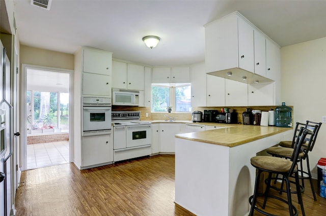 kitchen featuring white appliances, a kitchen breakfast bar, kitchen peninsula, dark hardwood / wood-style flooring, and white cabinetry