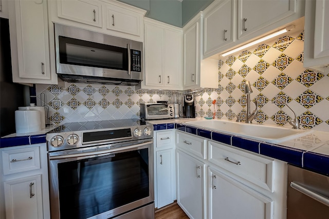 kitchen with appliances with stainless steel finishes, sink, tasteful backsplash, white cabinetry, and hardwood / wood-style floors