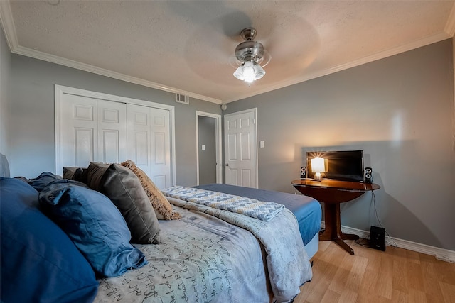 bedroom with a textured ceiling, a closet, light hardwood / wood-style flooring, ornamental molding, and ceiling fan