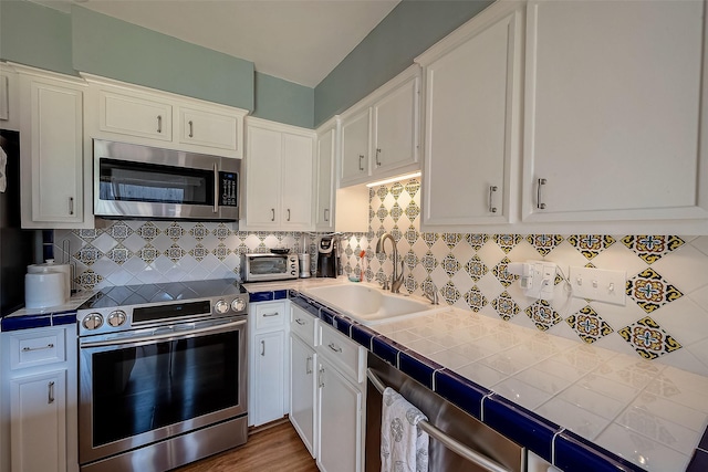 kitchen with sink, stainless steel appliances, white cabinetry, and tile counters