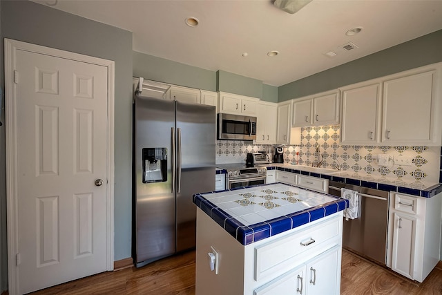 kitchen featuring appliances with stainless steel finishes, tile counters, a kitchen island, white cabinetry, and hardwood / wood-style flooring