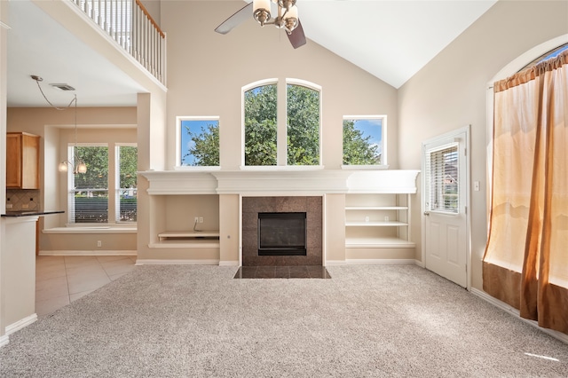 unfurnished living room with a tiled fireplace, ceiling fan, light colored carpet, and plenty of natural light