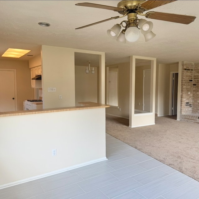 kitchen with light carpet, gas range gas stove, ceiling fan, and a textured ceiling