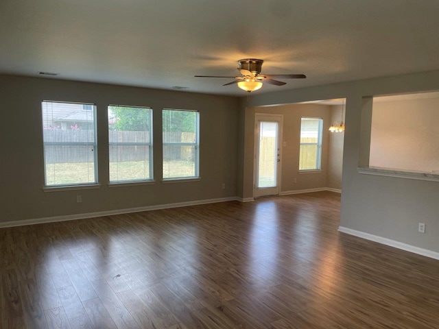 spare room featuring dark hardwood / wood-style flooring, plenty of natural light, and ceiling fan with notable chandelier