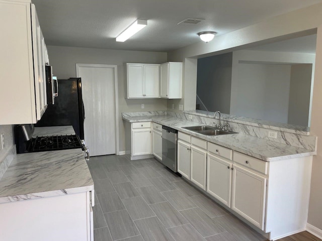 kitchen with white cabinets, sink, appliances with stainless steel finishes, light stone counters, and kitchen peninsula