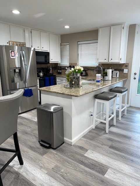 kitchen with white cabinets, backsplash, light hardwood / wood-style floors, and stainless steel fridge