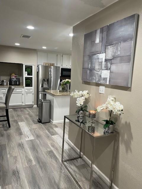 kitchen with black microwave, white cabinetry, light wood finished floors, and stainless steel fridge with ice dispenser