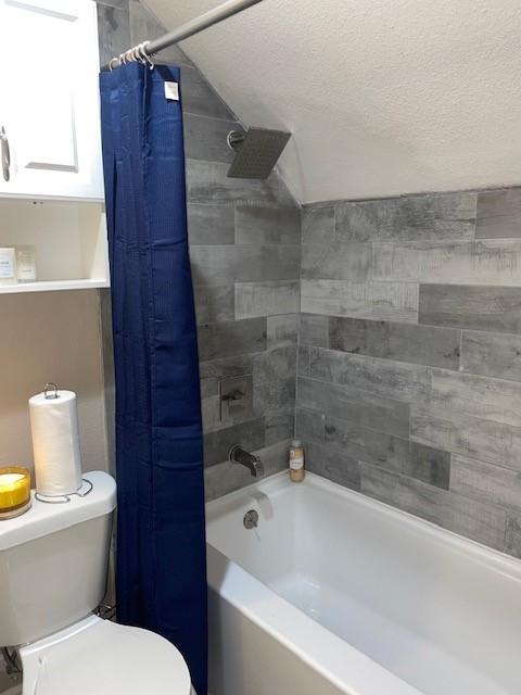 bathroom with shower / bath combo, vaulted ceiling, a textured ceiling, and toilet