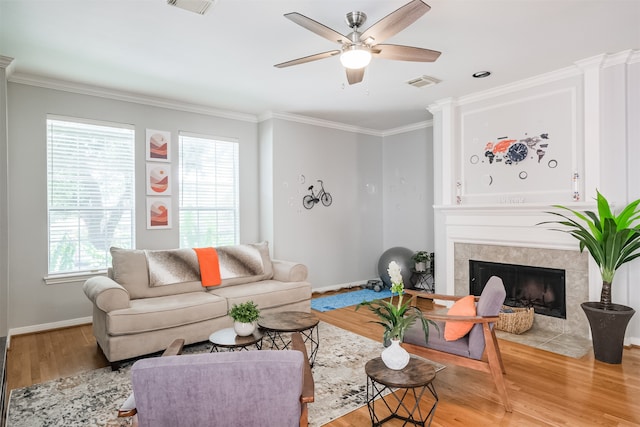 living room with light wood-type flooring, ceiling fan, a high end fireplace, and ornamental molding