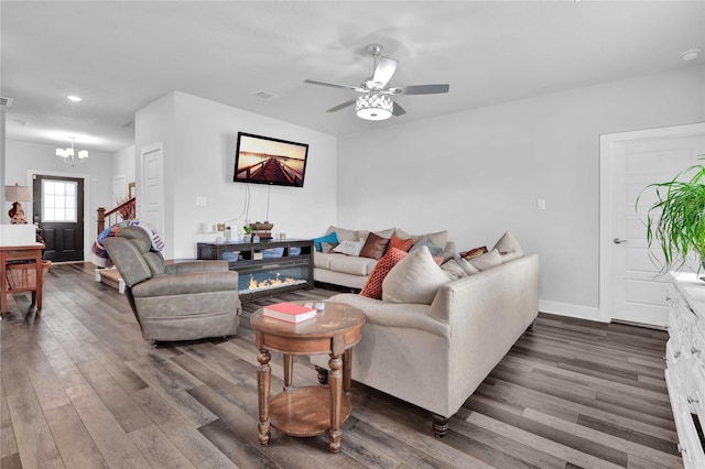 living room with ceiling fan with notable chandelier and dark hardwood / wood-style flooring