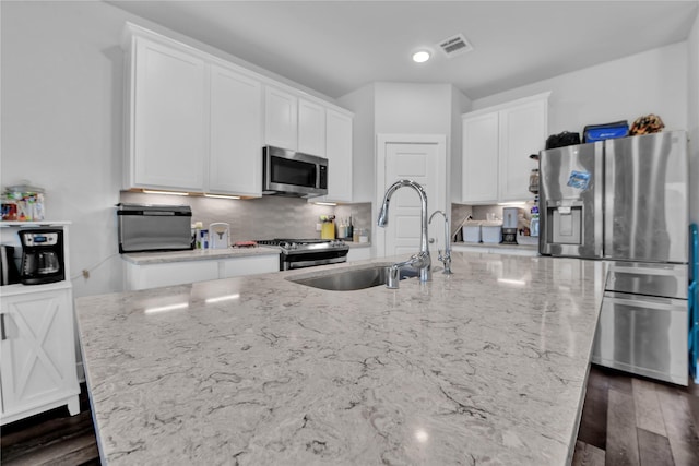 kitchen featuring white cabinetry, an island with sink, sink, stainless steel appliances, and light stone countertops