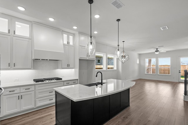 kitchen featuring ceiling fan with notable chandelier, a center island with sink, white cabinetry, and custom exhaust hood