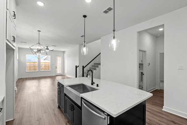 kitchen with white cabinetry, sink, stainless steel dishwasher, wood-type flooring, and a center island with sink