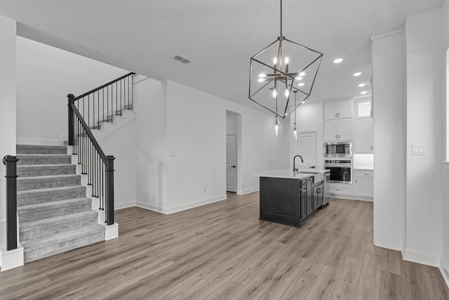 kitchen with a kitchen island with sink, white cabinets, sink, light hardwood / wood-style flooring, and stainless steel appliances