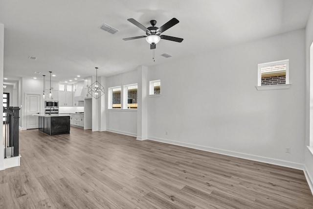 unfurnished living room featuring hardwood / wood-style floors and ceiling fan with notable chandelier