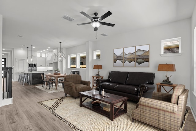 living room featuring ceiling fan with notable chandelier and light hardwood / wood-style floors