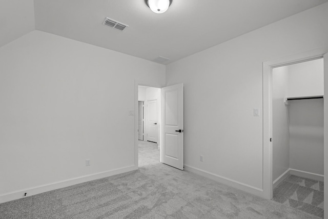 unfurnished bedroom with a walk in closet, light colored carpet, vaulted ceiling, and a closet