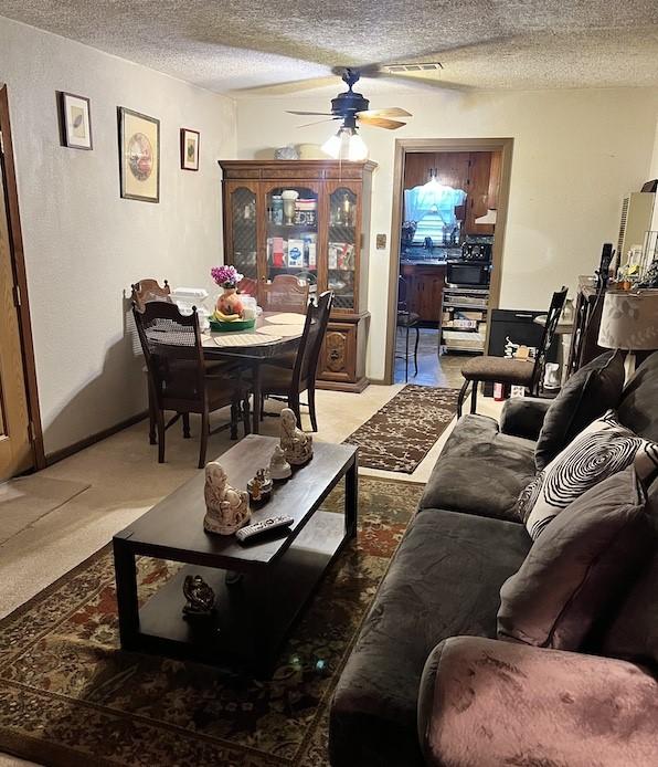 living room with ceiling fan, carpet floors, and a textured ceiling