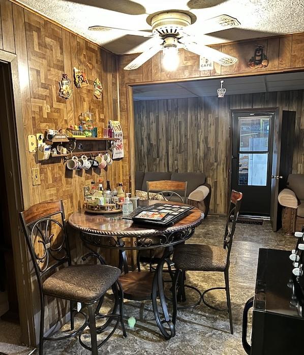 dining area featuring ceiling fan, wood walls, and bar